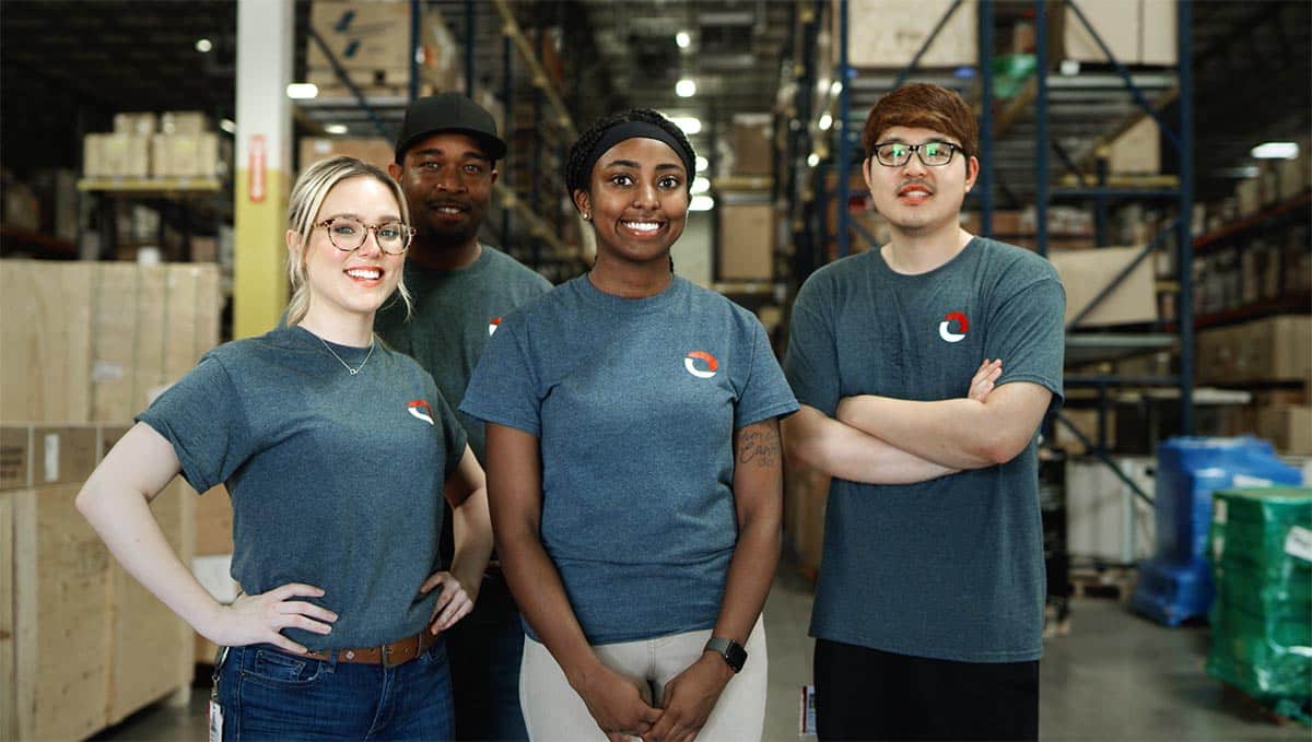 Four logistics workers wearing Omni shirts standing in front of racks in warehouse